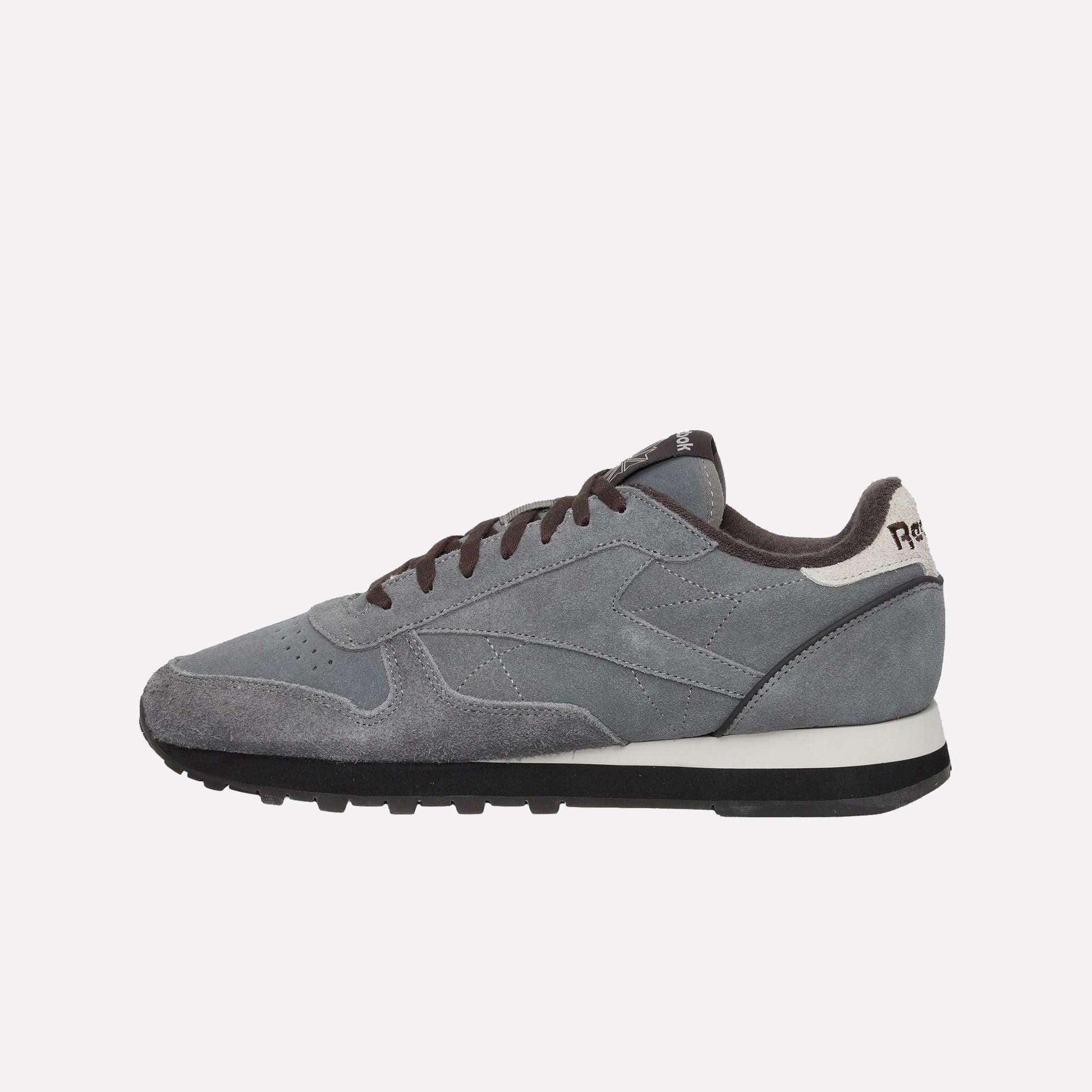 The Reebok Classic Leather Premium LTD Shoes feature gray suede uppers with black laces and sole, a white heel accent, and visible stitching—perfect for fans of classic style. Shown here on a light blue background.