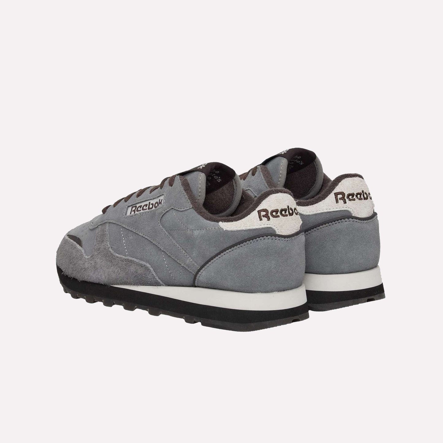 A pair of Reebok Classic Leather Premium LTD Shoes in gray, featuring white soles and black bottoms, are displayed on a light blue background with back and side views that highlight their retro, timeless silhouette.