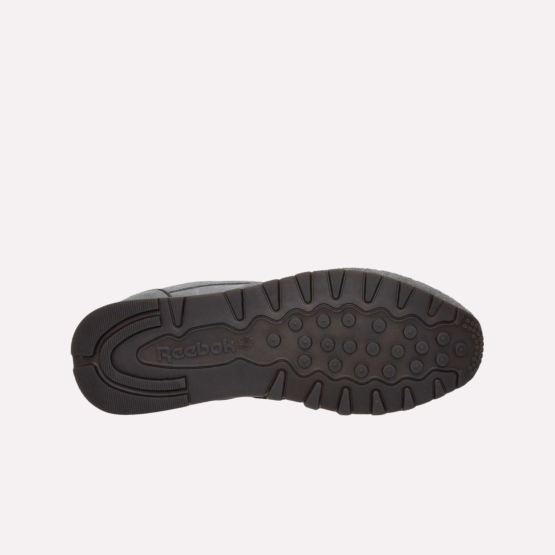 The image displays the black rubber sole of Reebok Classic Leather Premium LTD Shoes facing up on a light blue background, highlighting the textured tread pattern, classic silhouette, and visible Reebok logo.