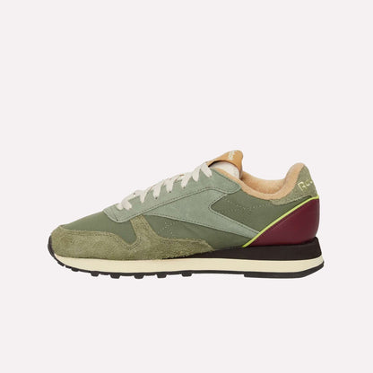 A side-profile view of the Reebok Classic Leather Premium LTD Shoes features green suede and fabric uppers, white laces, beige lining, a black and white sole, and a burgundy heel accent—a fresh update on the classic silhouette.