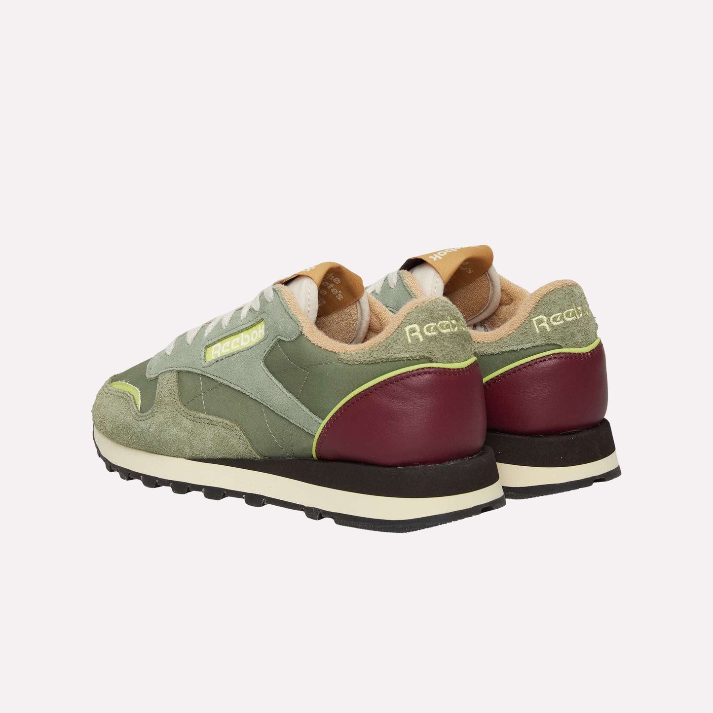 The Reebok Classic Leather Premium LTD Shoes are retro sneakers with green suede and mesh uppers, maroon heel accents, yellow branding, a classic silhouette, white laces, and beige interior lining—shown from the back and side.