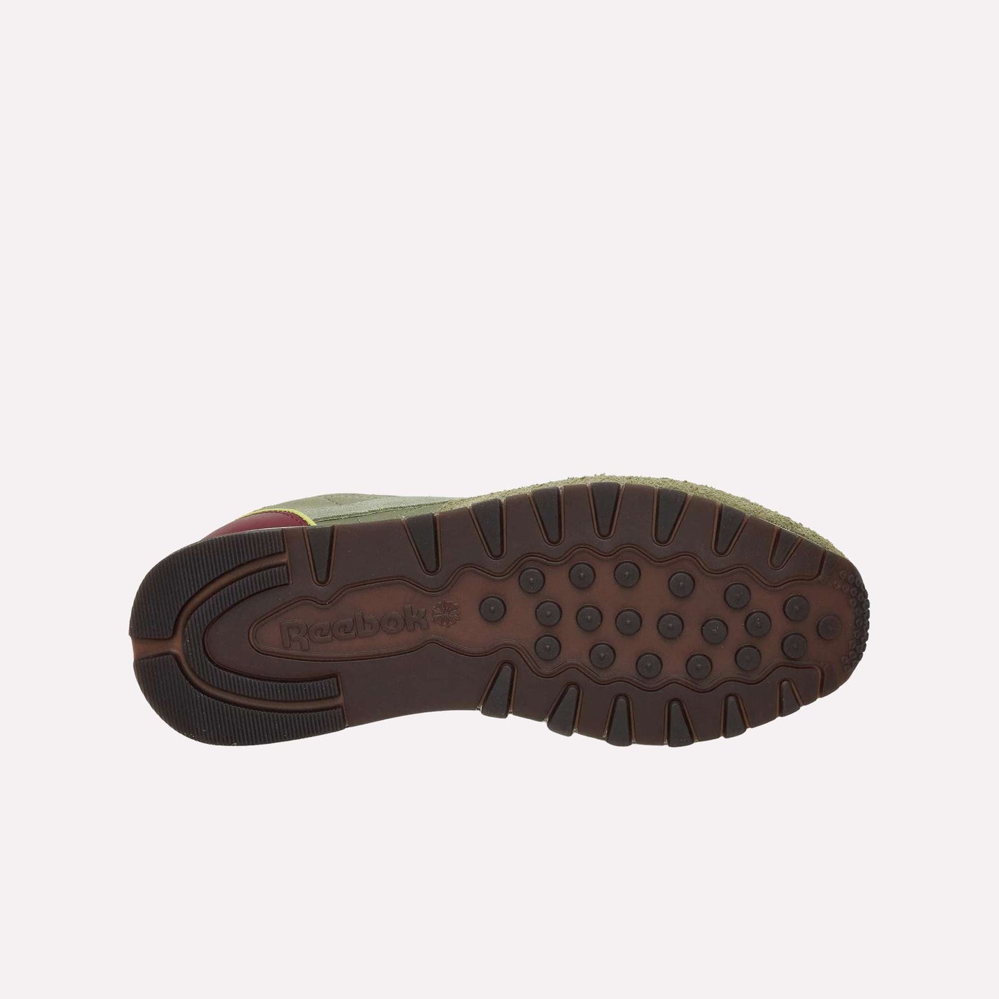 The image shows the bottom view of Reebok Classic Leather Premium LTD Shoes with a brown rubber sole featuring circular treads and the Reebok logo. The retro sneakers have a green upper and a touch of maroon near the heel.