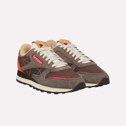 A pair of Reebok Classic Leather Premium LTD Shoes in brown with beige, red, and cream accents. These retro sneakers have white laces, a suede and mesh upper, chunky black sole, and the iconic Reebok logo on the side.