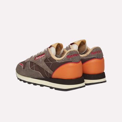 A pair of Reebok Classic Leather Premium LTD Shoes shown from the back and side, with brown suede and leather panels, orange heel accents, beige lining, and red Reebok branding—retro sneakers with a classic silhouette.