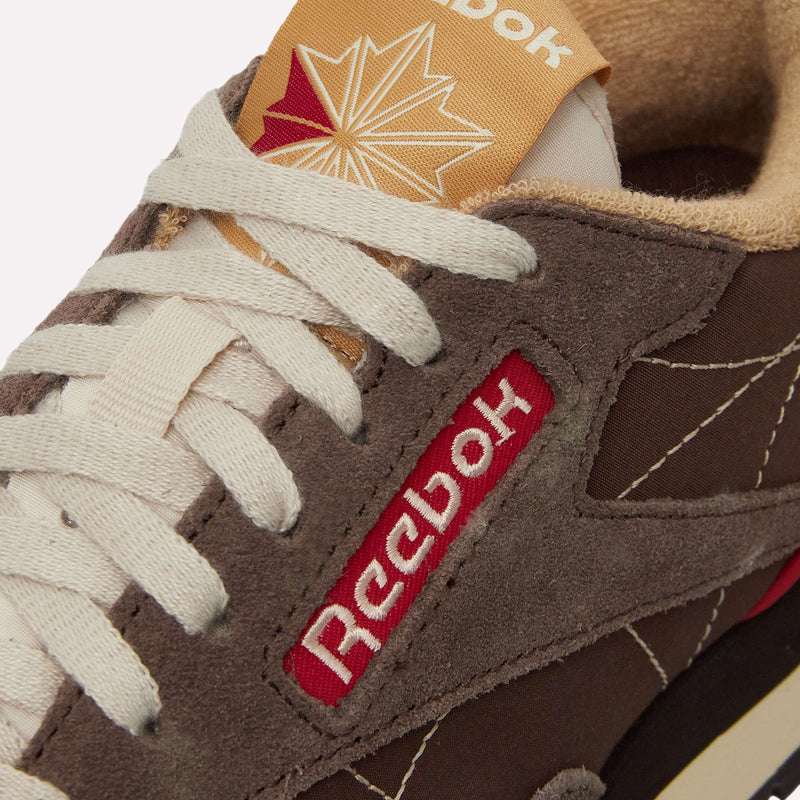 Close-up of brown Reebok Classic Leather Premium LTD Shoes, featuring white laces, a red Reebok logo on the side, and a beige tongue with a red starburst—highlighting the iconic silhouette of these retro sneakers.