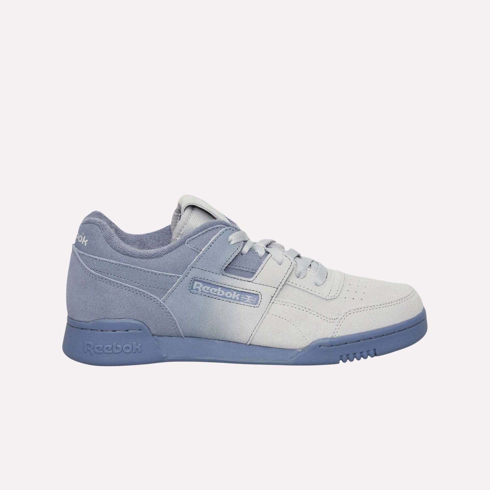 The Reebok Workout Plus OG Shoes in light grey and lavender are shown from the side on a solid light blue background, highlighting their suede and leather textures, classic silhouette, and signature Reebok branding on the side.