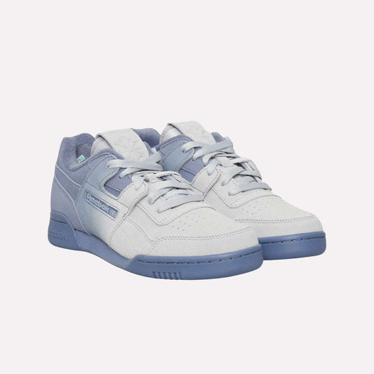 A pair of light grey and blue Reebok Workout Plus OG Shoes with suede texture, blue soles, and laces showcases a classic silhouette against a light blue background.