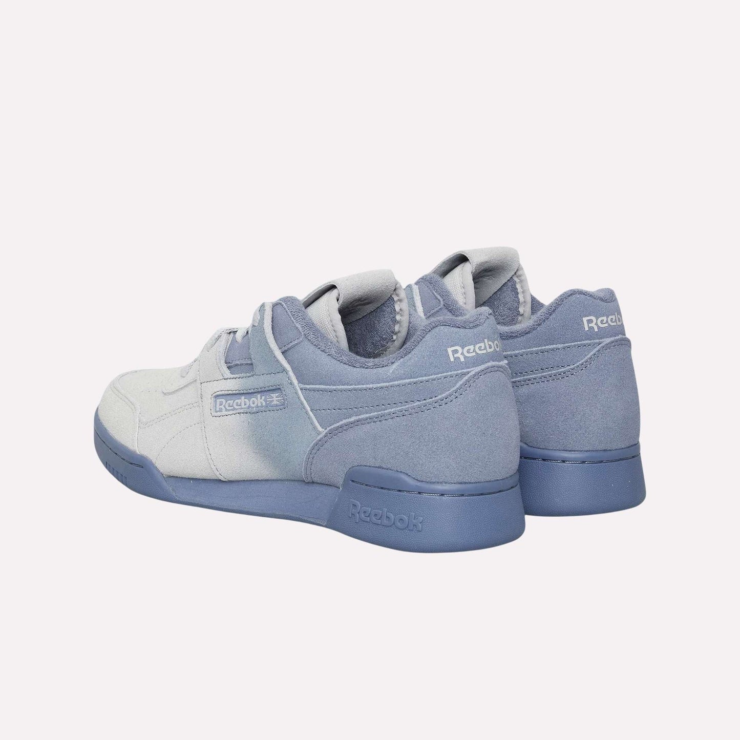 A pair of Reebok Workout Plus OG Shoes in light blue and gray are displayed on a light blue background, showing back and side views with visible Reebok logos that highlight the classic silhouette.