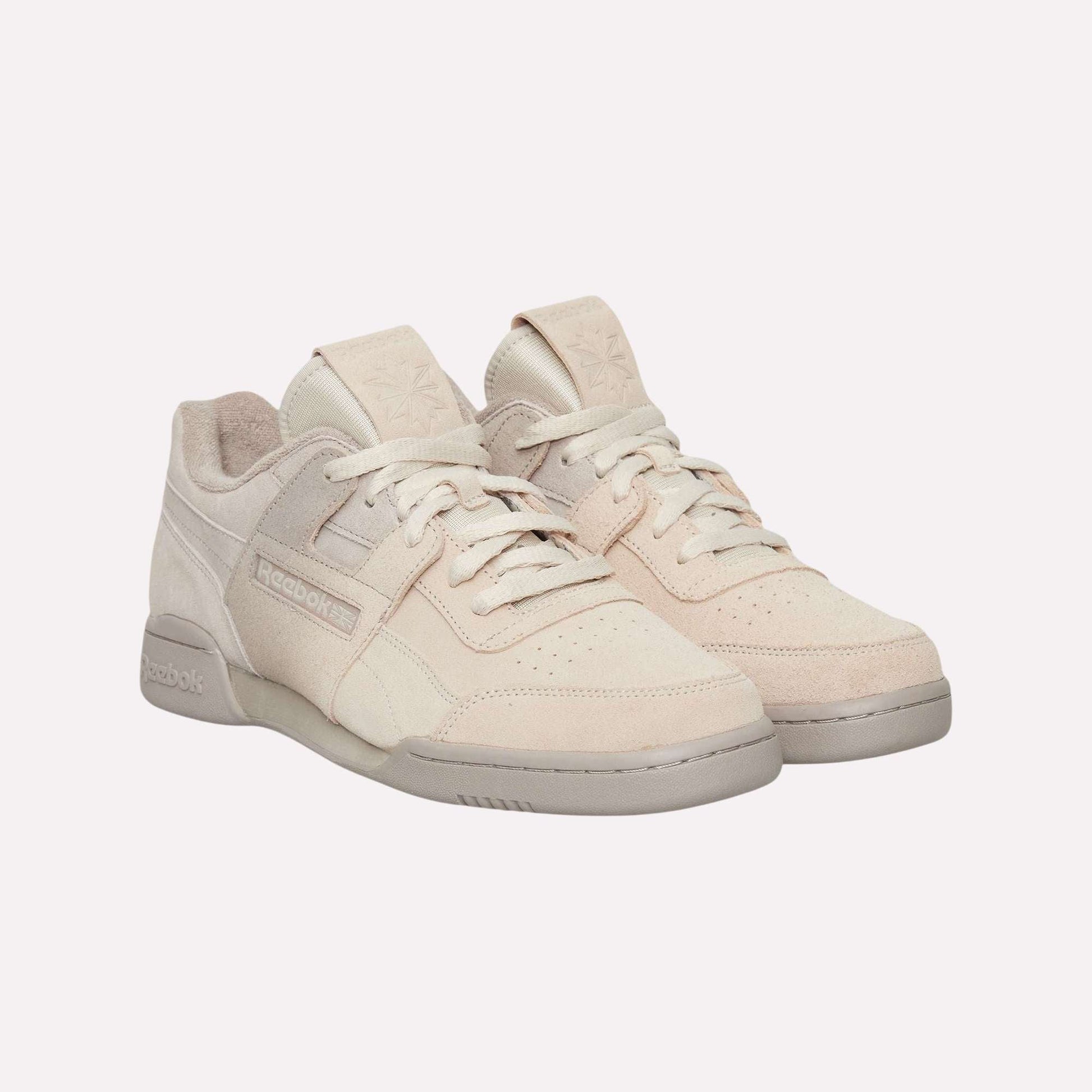 A pair of Reebok Workout Plus Og Shoes in light beige with suede uppers and light gray soles, showcasing a classic silhouette, displayed on a plain light blue background.