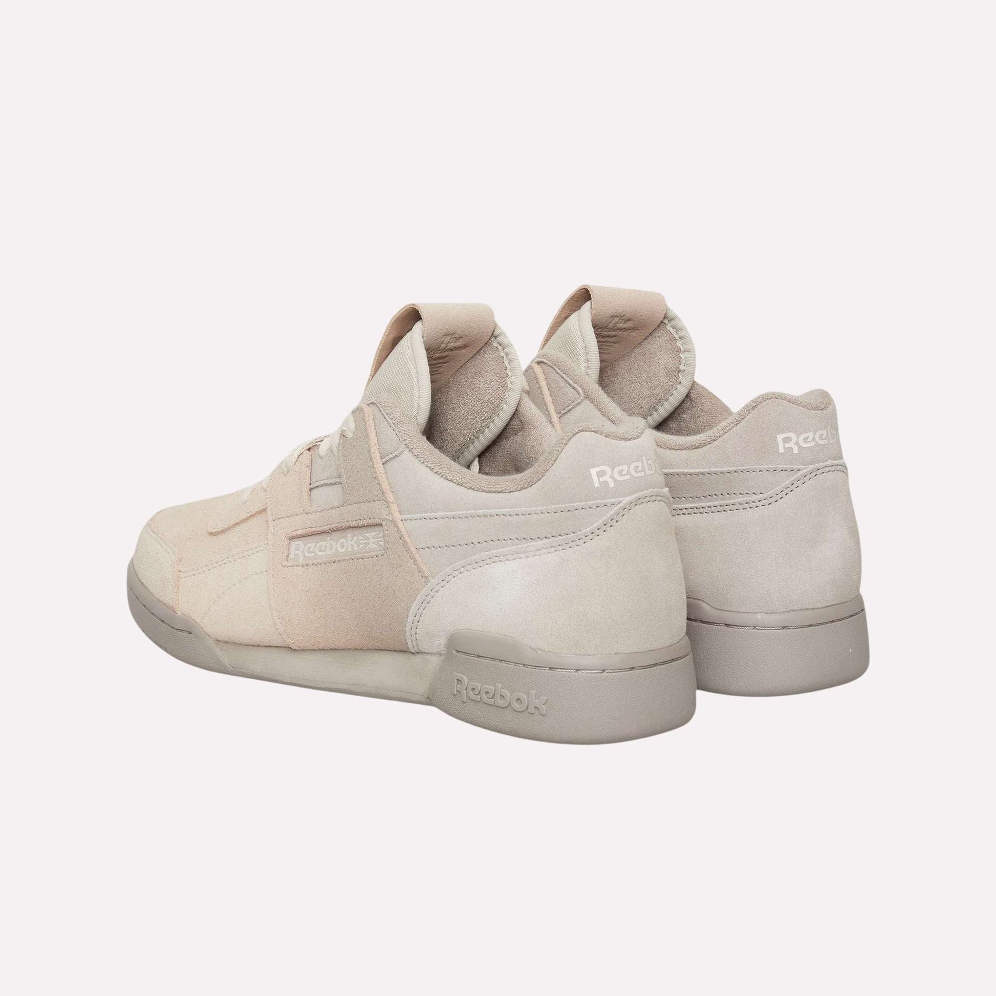 A pair of beige Reebok Workout Plus OG Shoes with suede accents is displayed against a light blue background, featuring one shoe angled to highlight the classic silhouette and Reebok side branding.
