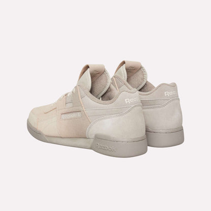A pair of beige Reebok Workout Plus OG Shoes with suede accents is displayed against a light blue background, featuring one shoe angled to highlight the classic silhouette and Reebok side branding.