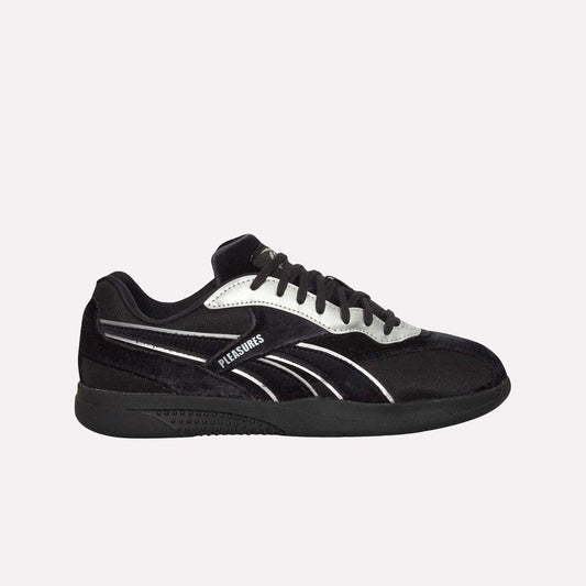 The Reebok Pleasures Hammer Street Shoes, a black sneaker with a velvet upper and white and silver accents, features "PLEASURES" on the side—part of the PLEASURES collaboration—set against a plain light blue background.