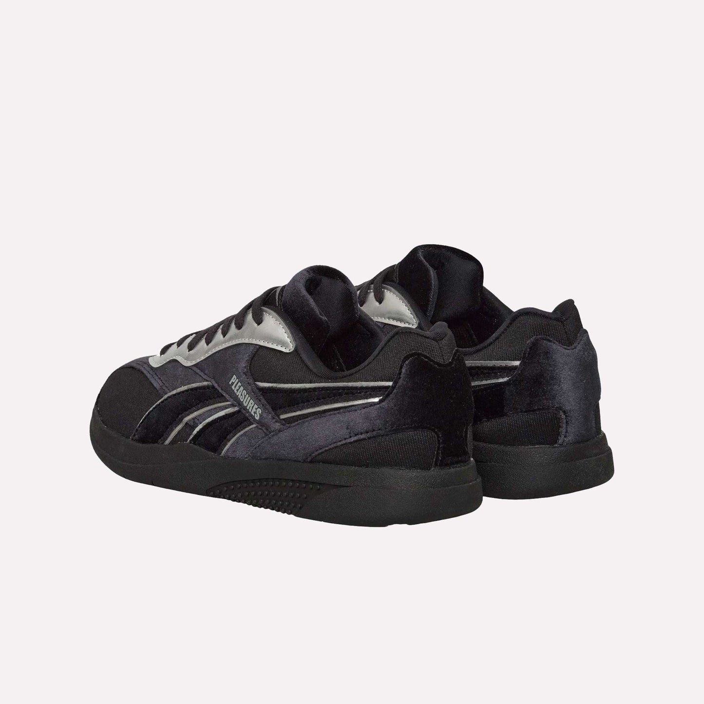 The Reebok Pleasures Hammer Street Shoes, black and silver with a velvet upper and black soles, are displayed from back and side angles against a light blue background.