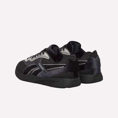 The Reebok Pleasures Hammer Street Shoes, black and silver with a velvet upper and black soles, are displayed from back and side angles against a light blue background.