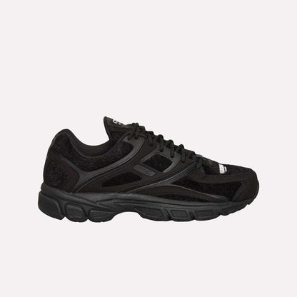 The Reebok Pleasures Premier Trinity KFS Shoes feature a black athletic design with mesh and suede details, black laces, a textured rubber sole, and subtle Reebok branding. Displayed on a light blue background.