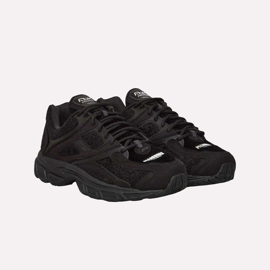 The Reebok Pleasures Premier Trinity KFS Shoes are black athletic sneakers with thick soles, mesh accents, and a unique pony hair upper, displayed on a plain light blue background.