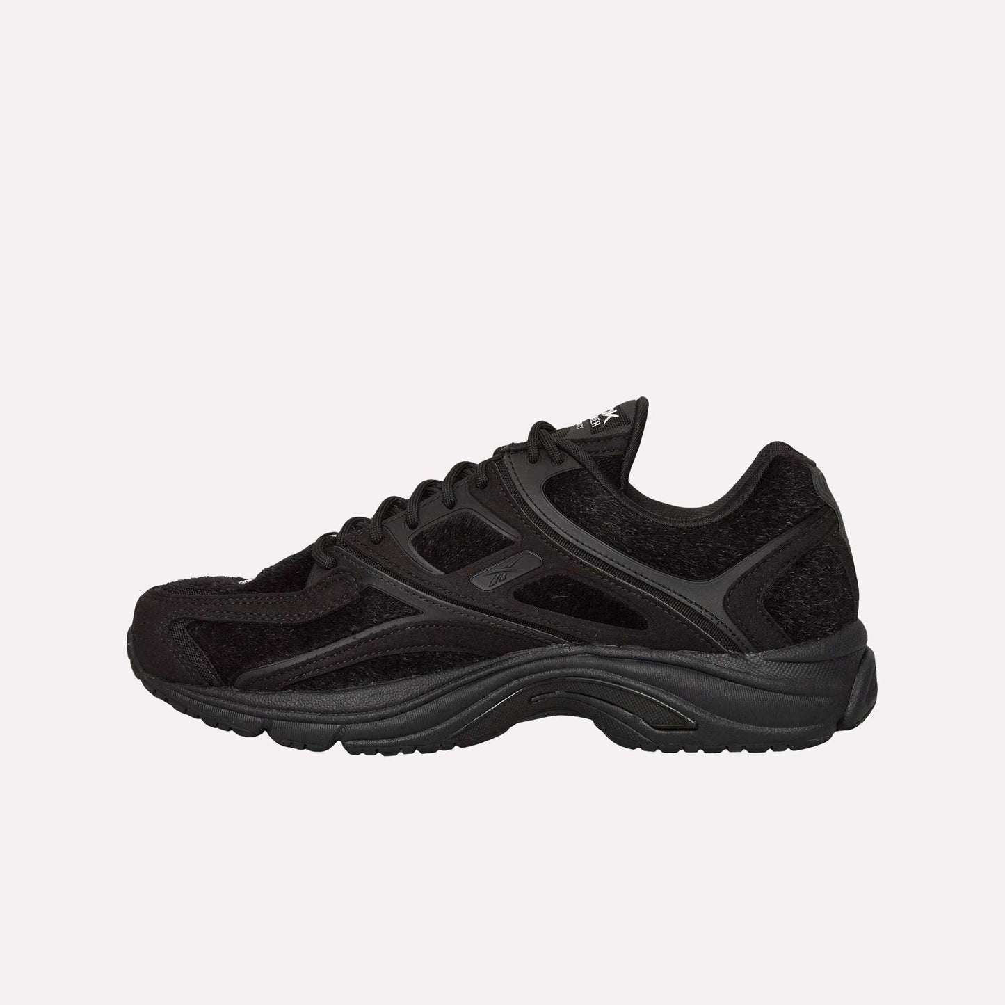 The Reebok Pleasures Premier Trinity KFS Shoes feature a black textured pony hair upper and thick sole, showcased in profile on a light blue background—a striking release from the latest Pleasures collaboration.