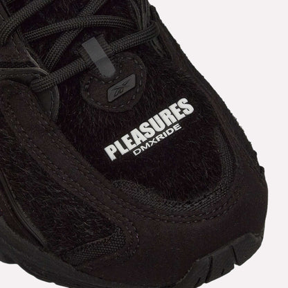 Close-up of the Pleasures Premier Trinity KFS Shoes from Reebok, featuring a black textured pony hair upper. "PLEASURES" stands out in bold white with DMXRIDE underneath. Finished with black laces and stitching for a striking look.