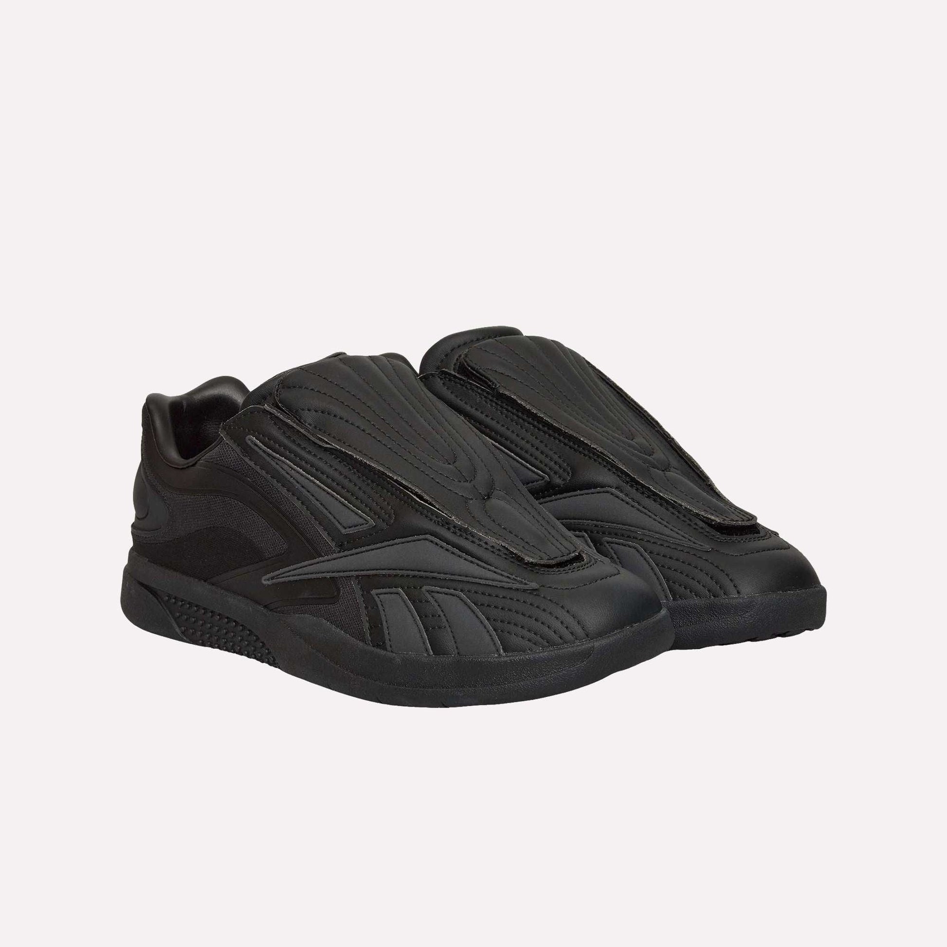 A pair of Reebok Hammer Pro Ltd sneakers in black, featuring a futuristic sculpted design, hidden laces, and durable rubber soles, are displayed side by side on a white background.