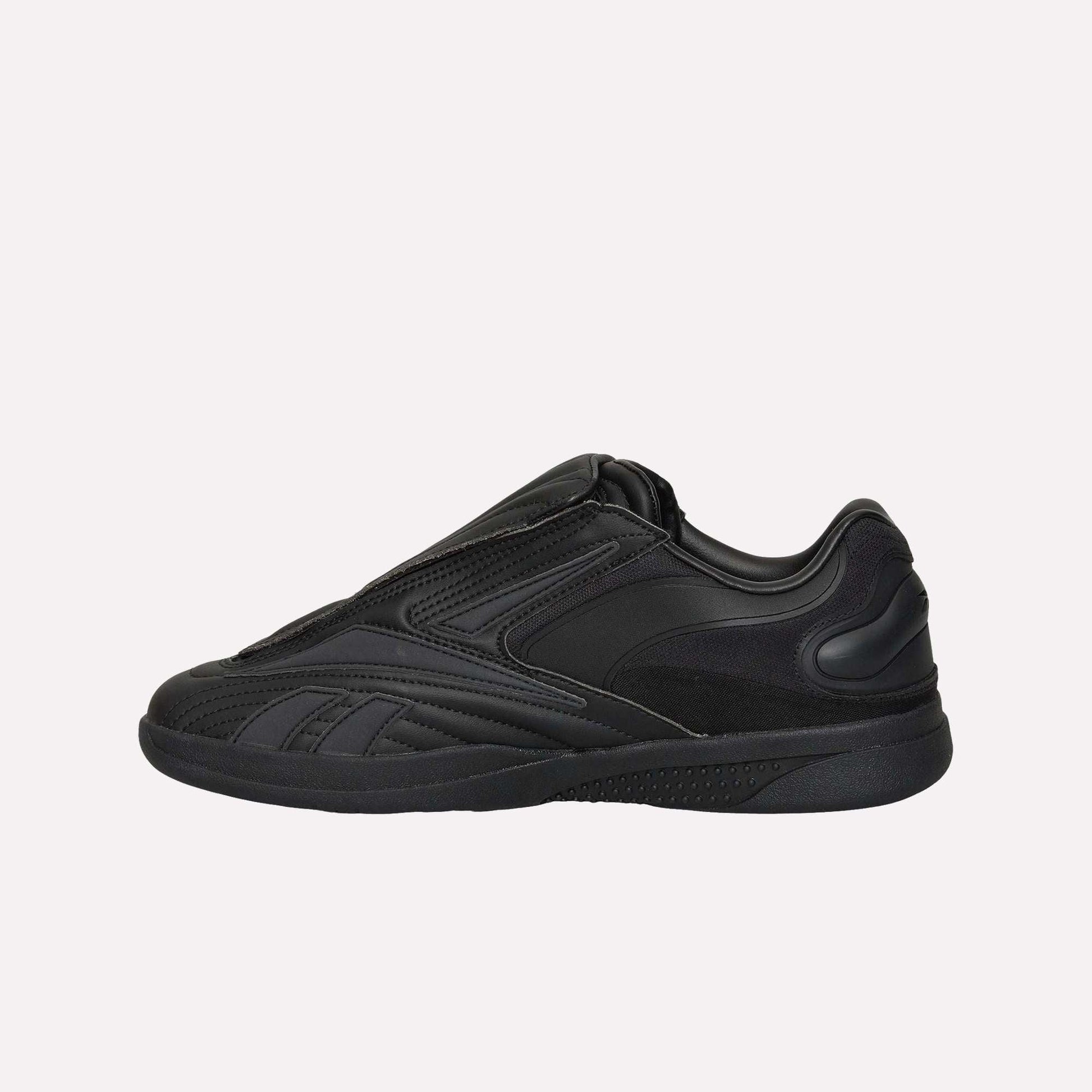 The Reebok Hammer Pro Ltd sneaker features a sleek, all-black design with a low profile, suede upper, textured and smooth panels, and a thick rubber sole. Shown in side view against a white background.