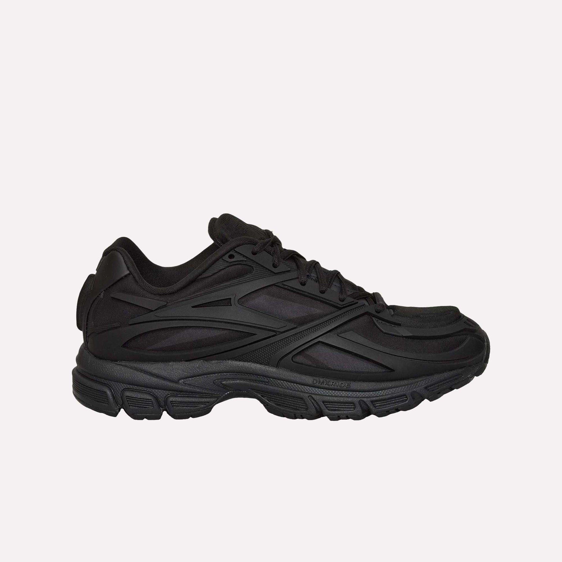 A black Reebok Premier Road Modern running shoe with a chunky sole and layered, textured side details is shown from the left against a white background.