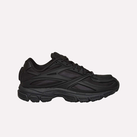 A black Reebok Premier Road Modern running shoe with a chunky sole and layered, textured side details is shown from the left against a white background.