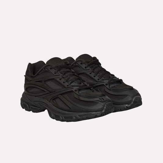 A pair of Reebok Premier Road Modern running shoes in all-black with textured soles, layered panels, and lace-up fronts, displayed side by side on a plain white background.