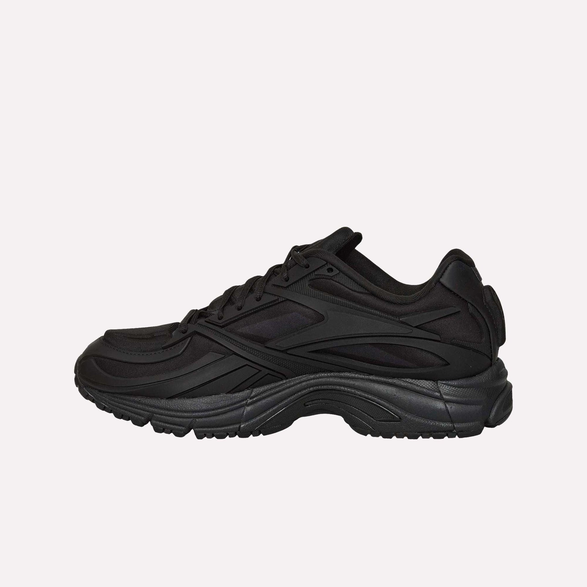 The Reebok Premier Road Modern running shoe in black features a textured sole, mesh and synthetic upper, and curved design lines, shown in side profile against a white background.