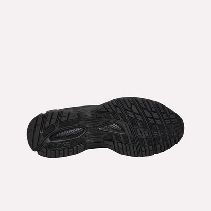 The image displays the black rubber sole of the Reebok Premier Road Modern, with textured patterns, grooves for traction, a dual-density midsole for comfort, and the Reebok logo by the arch.