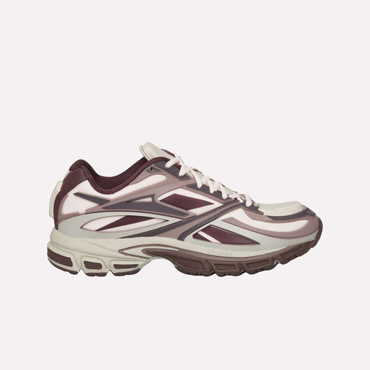 The Reebok Premier Road Modern sneaker features a beige and maroon colorway, dynamic angular patterns, and a thick dual-density midsole for grip. Shown in side profile on a white background.