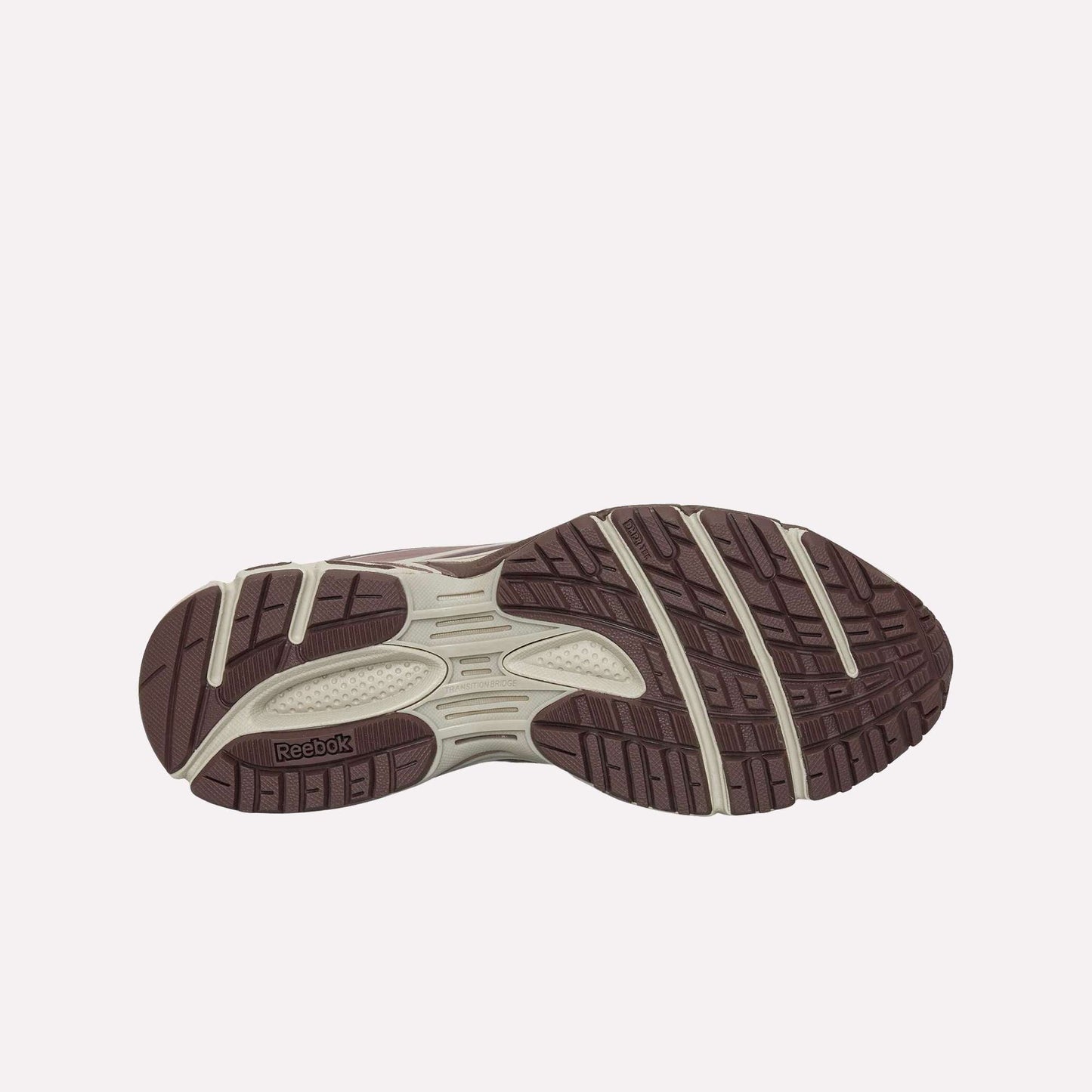The image displays the outsole of the Reebok Premier Road Modern, showcasing a brown and beige pattern with textured grips for traction, a dual-density midsole for comfort, and the Reebok logo on the sole.