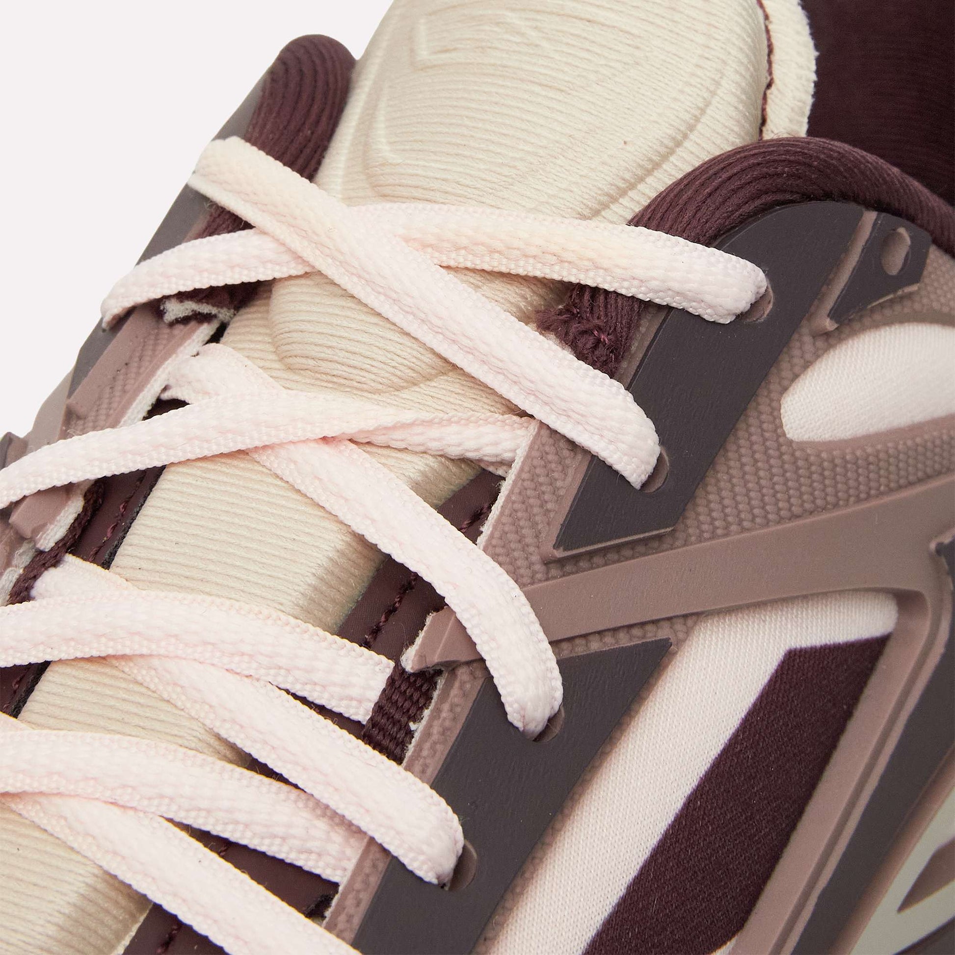 Close-up of the Reebok Premier Road Modern sneaker featuring cream laces, a beige tongue, maroon and brown overlays with textured materials, geometric accents, and a dual-density midsole inspired by classic Reebok running shoes.