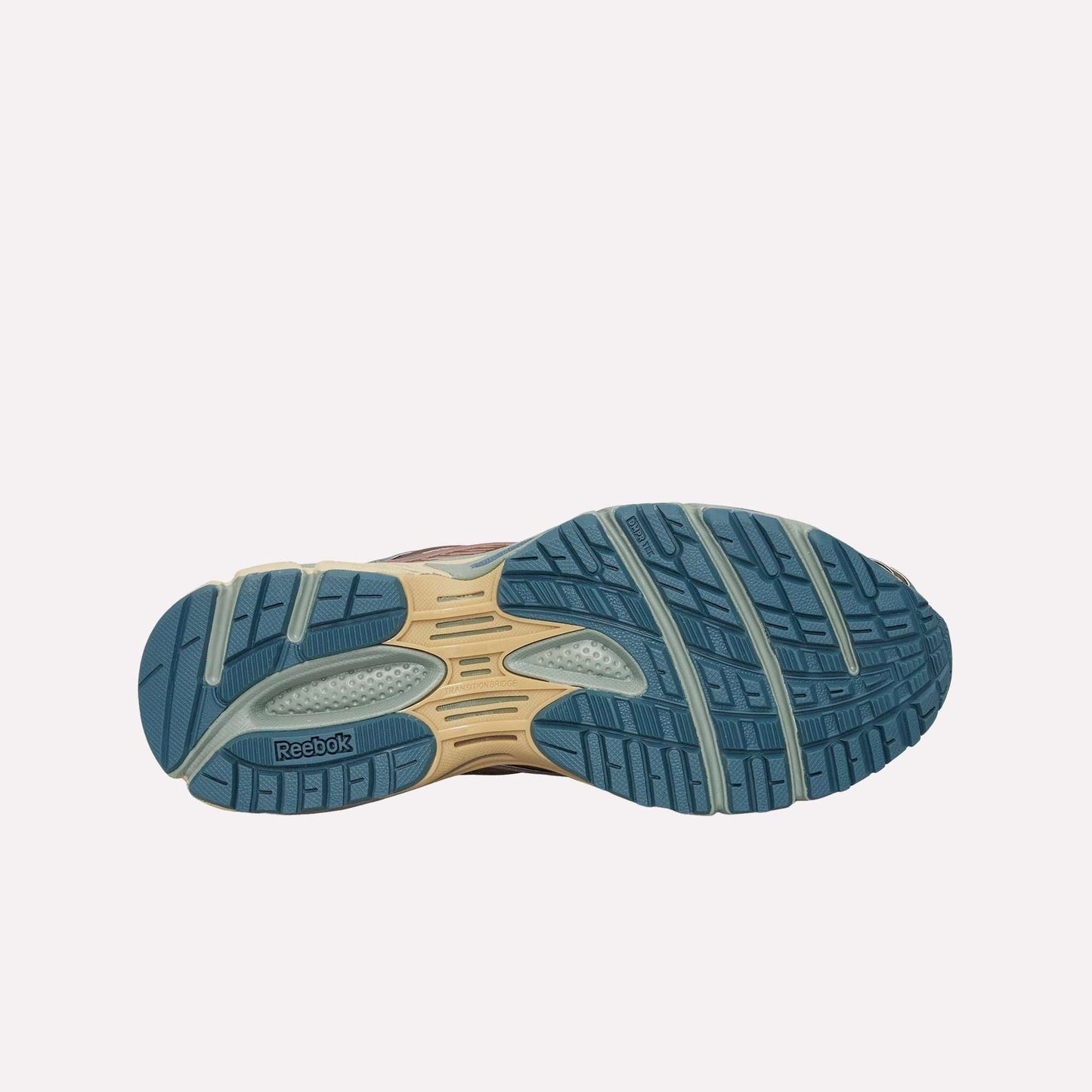 The image shows the blue and beige rubber outsole of the Reebok Premier Road Ultra, featuring textured treads and grooves for grip, with the Reebok logo on the left side.