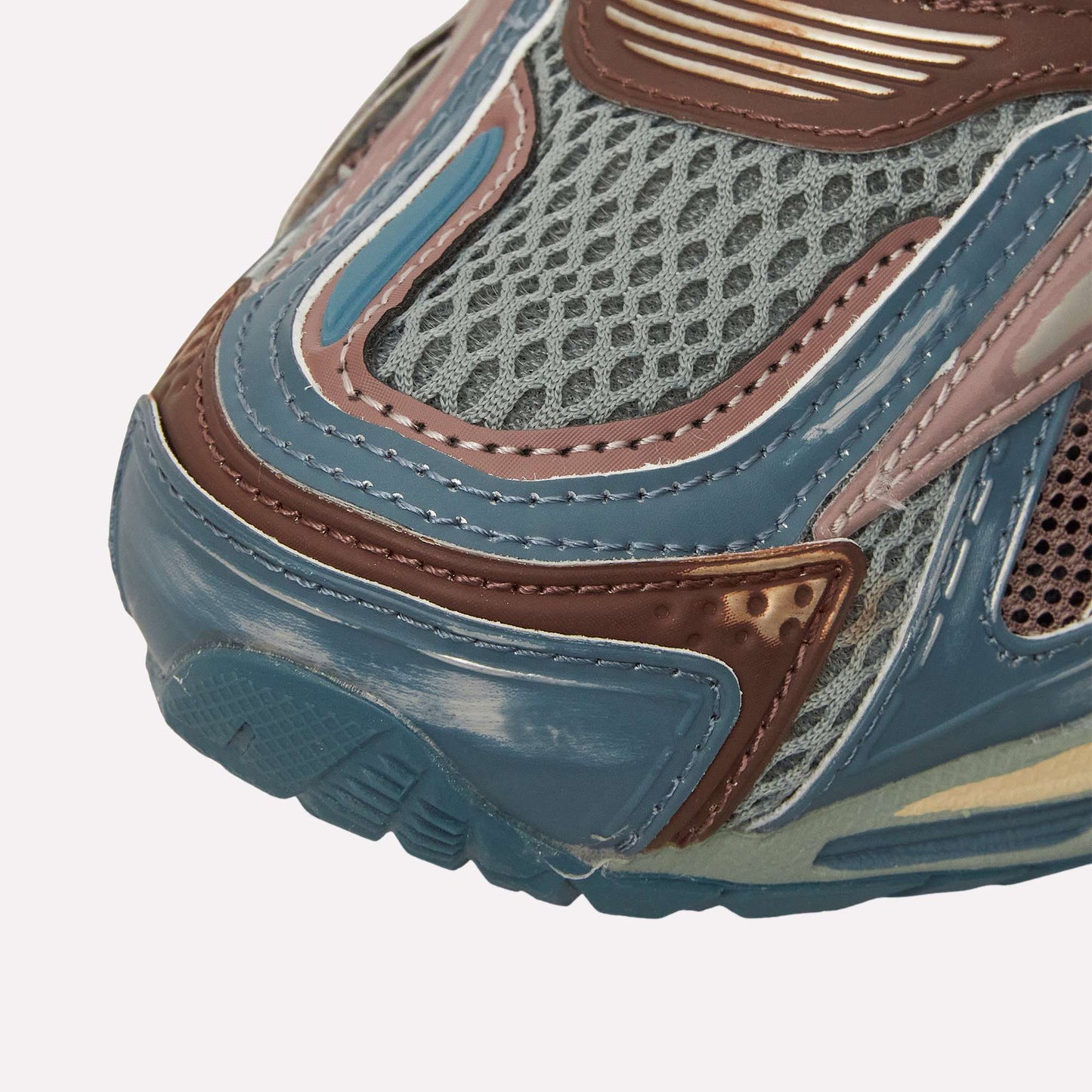 Close-up of the Reebok Premier Road Ultra toe area, showcasing a textured blue, brown, and gray design with mesh and layered synthetics, visible stitching, dual-density midsole detail, and treaded sole.
