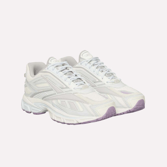 The Reebok Premier Road Ultra is a pair of white athletic sneakers with light grey and off-white accents, chunky soles, a dual-density midsole, light purple outsoles, and a modern sporty lace-up design.