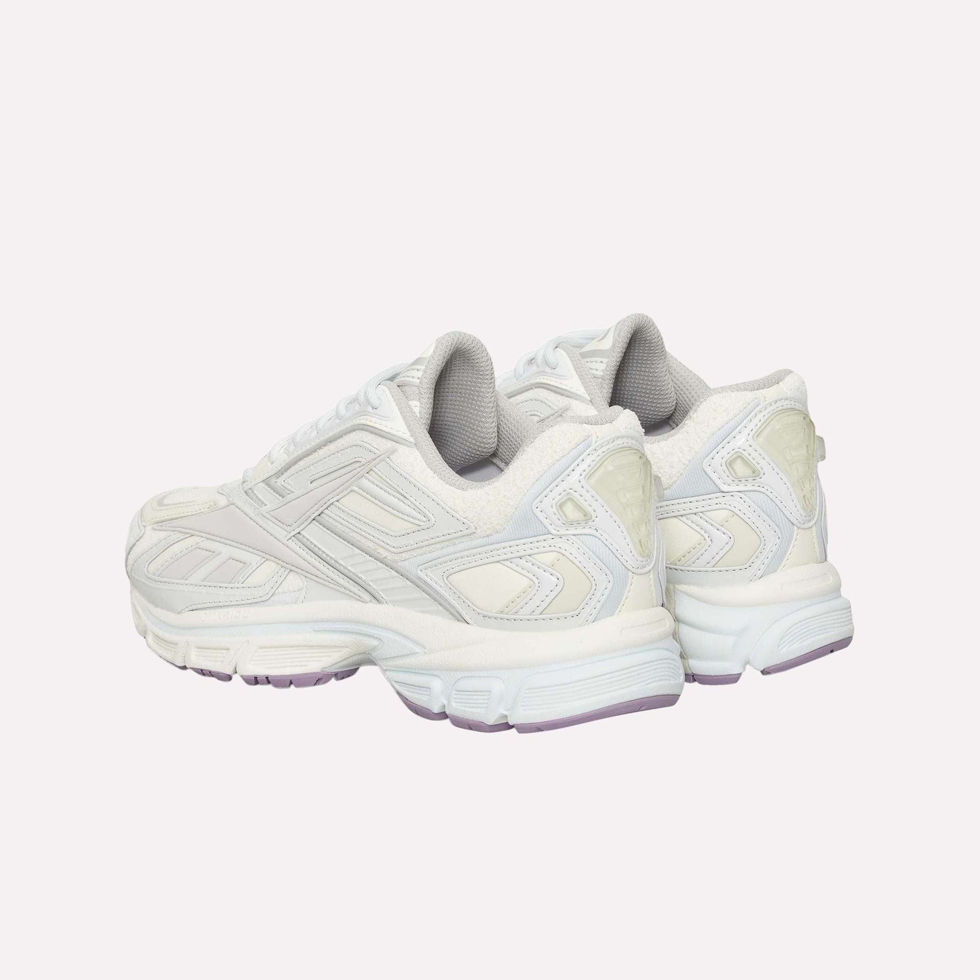 A pair of white Reebok Premier Road Ultra sneakers with light gray and off-white accents, viewed from the rear angle. Features include textured panels, a dual-density midsole, thick soles, and pale purple detailing on the outsole.