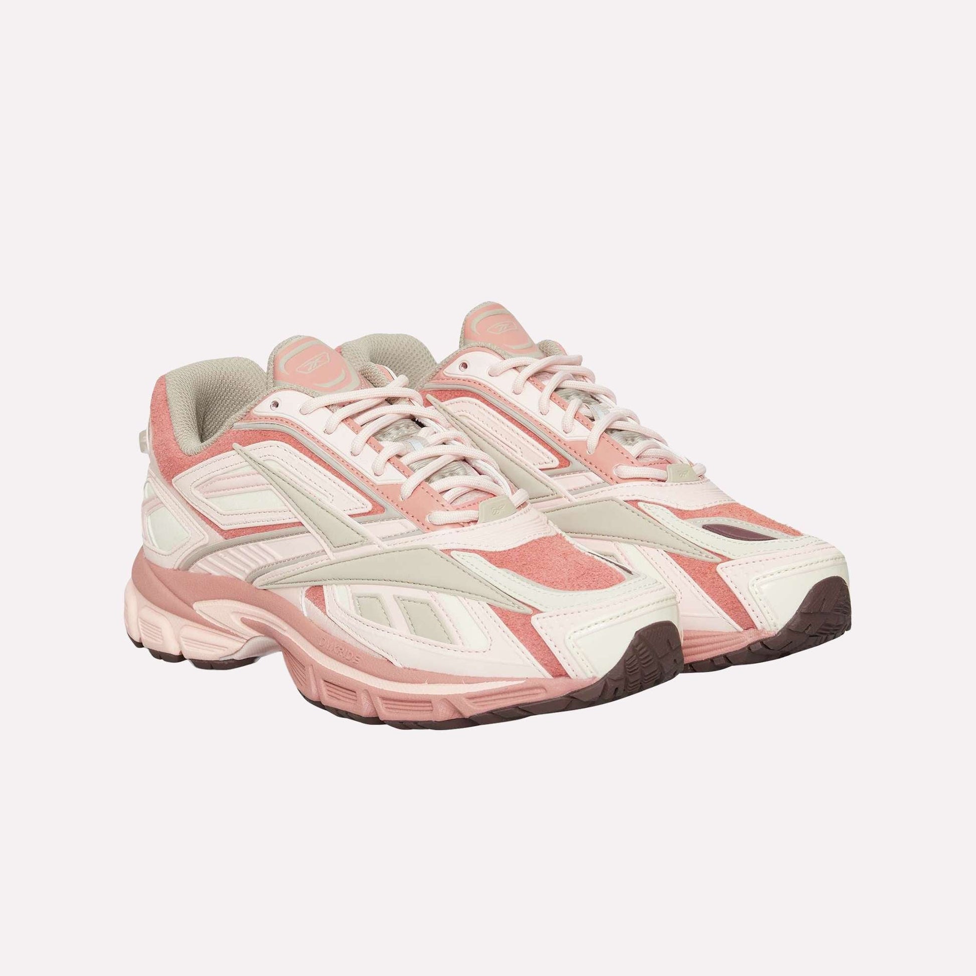 The Reebok Premier Road Ultra sneakers feature a pink, off-white, and cream color scheme, layered panels, white laces, and thick dual-density midsoles for comfort and support.