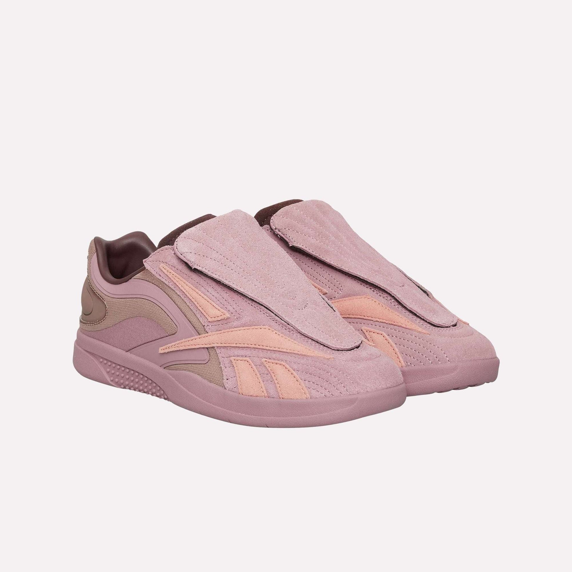The Reebok Hammer Pro Ltd sneakers feature mauve and pink suede uppers with large overlapping flaps over the laces, set on a light pink durable rubber sole.