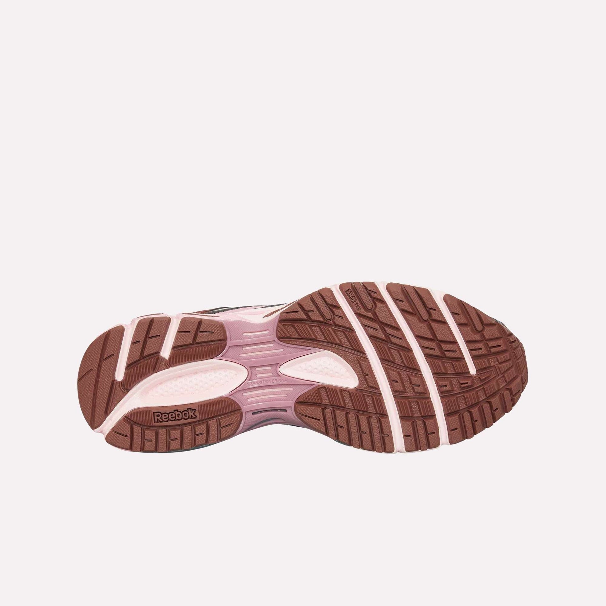 The image displays the sole of the Reebok Premier Road Ultra, featuring a brown, textured pattern with light pink accents and a visible heel logo. Its dual-density midsole offers enhanced support for athletic use.