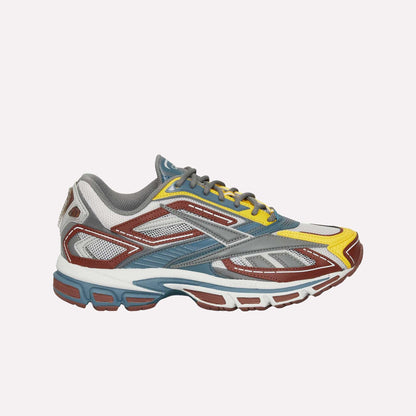 The Reebok Premier Road Ultra is a vibrant running sneaker with gray, white, yellow, and brown mesh and synthetic panels, blue accents, a multi-colored thick sole, and dual-density midsole. Side profile shown on white background.