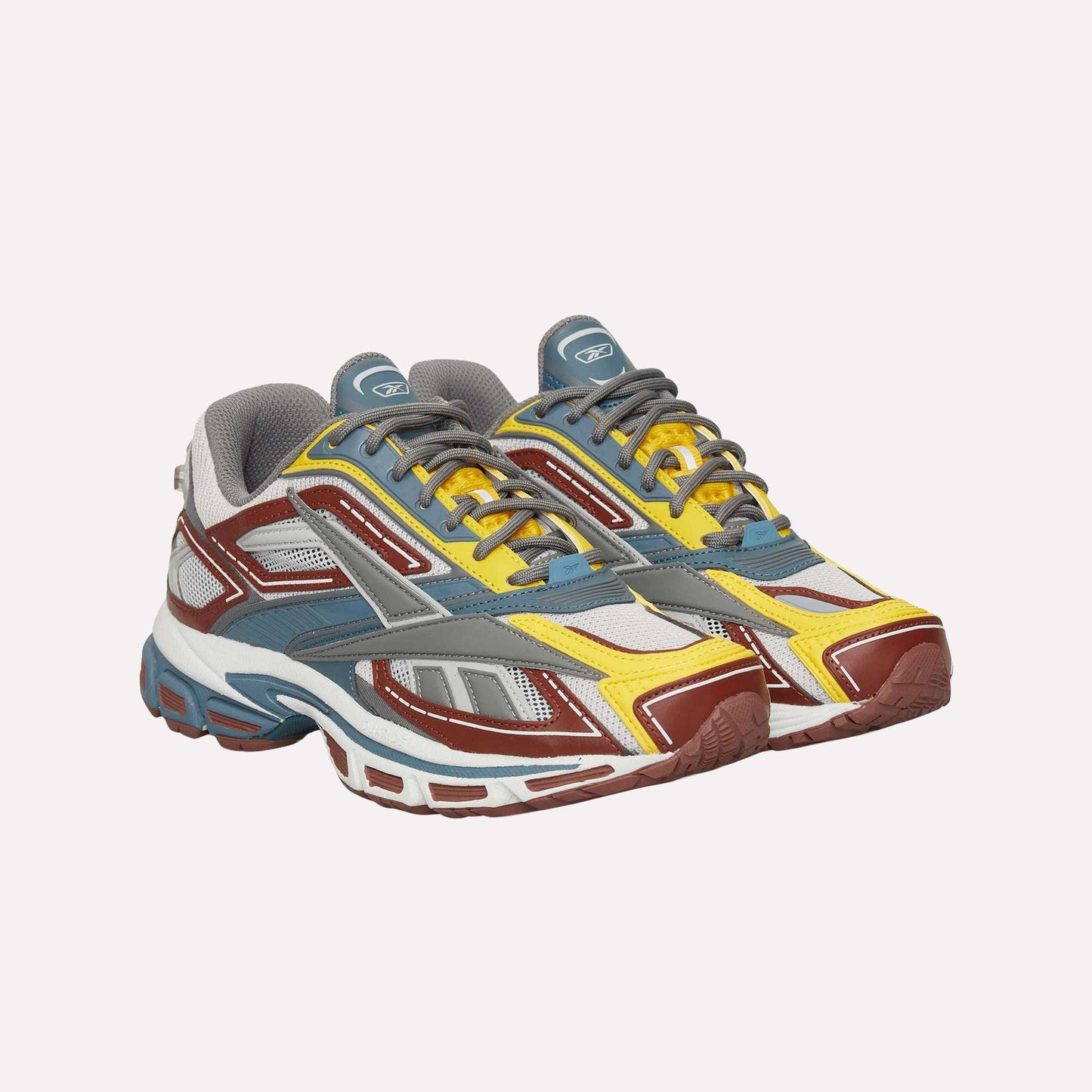 The Reebok Premier Road Ultra sneakers feature multicolored yellow, red, gray, white, and blue accents, a dual-density midsole, and gray laces, shown against a white background.