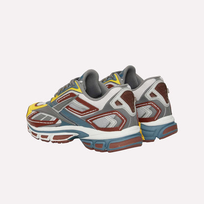A pair of Reebok Premier Road Ultra sneakers featuring multicolored yellow, brown, gray, white, and blue accents are shown side by side, highlighting the backs and sides of these archival running shoes.