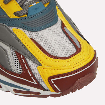 Close-up of the Reebok Premier Road Ultra shows mesh fabric, yellow, grey, blue, and brown overlays, visible stitching, and a textured rubber sole with dual-density midsole.