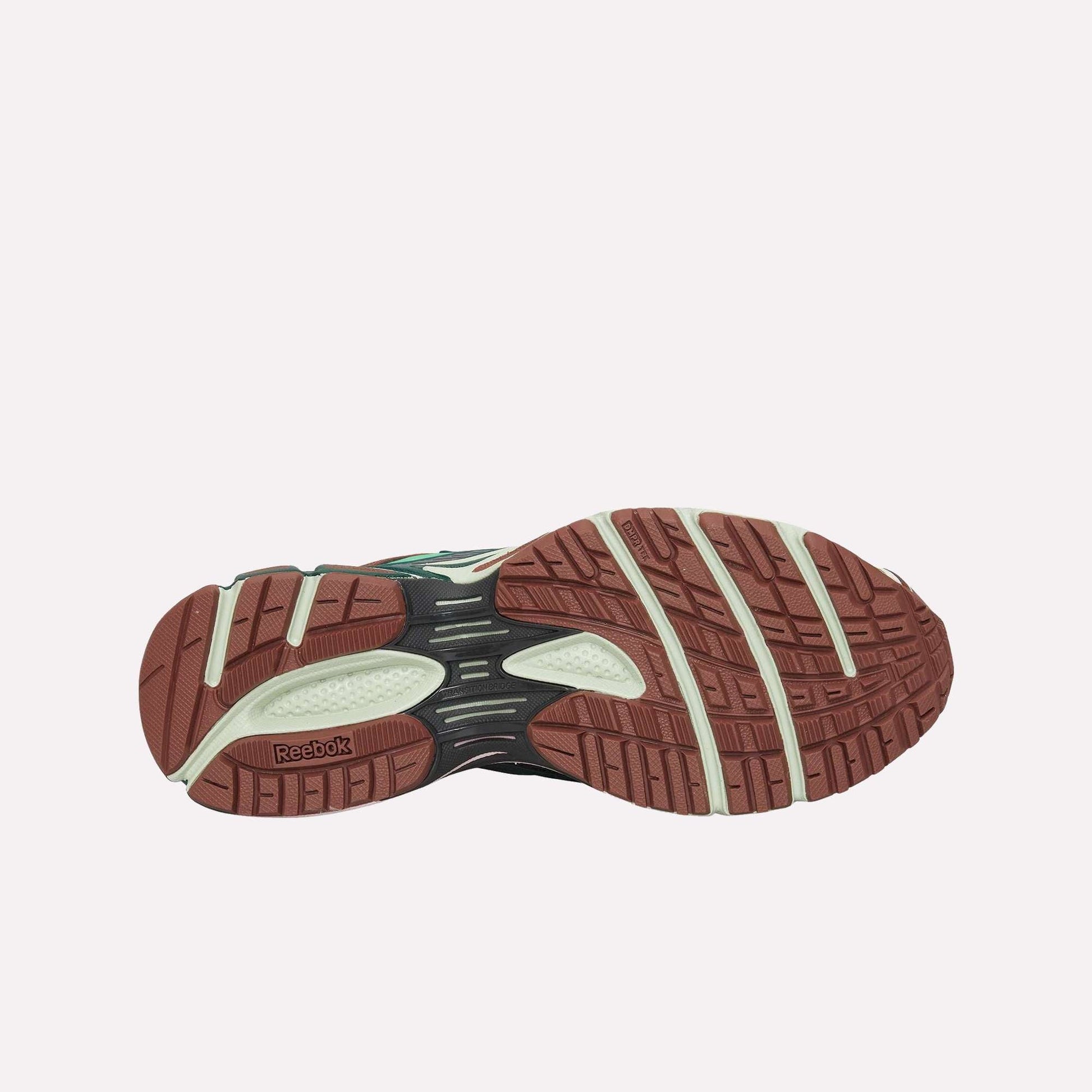 The image displays the sole of the Reebok Premier Road Ultra sneaker, featuring a brown and off-white traction pattern with visible Reebok branding and textured grooves for enhanced grip.