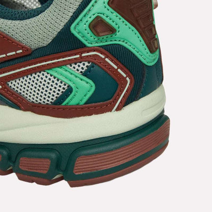 Close-up of the Reebok Premier Road Ultra heel and midsole, showcasing green, brown, off-white, and grey colors with mesh and synthetic overlays, intricate stitching, and a dual-density midsole.