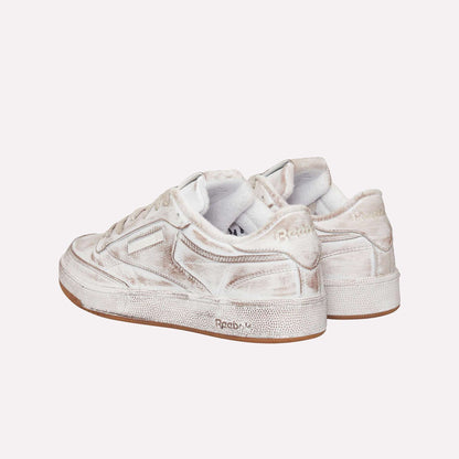 The Reebok Club C 85 Vintage sneakers feature an off-white upper, distressed textured details, and light brown rubber soles, shown at an angle highlighting the back and sides—a true lifestyle classic.