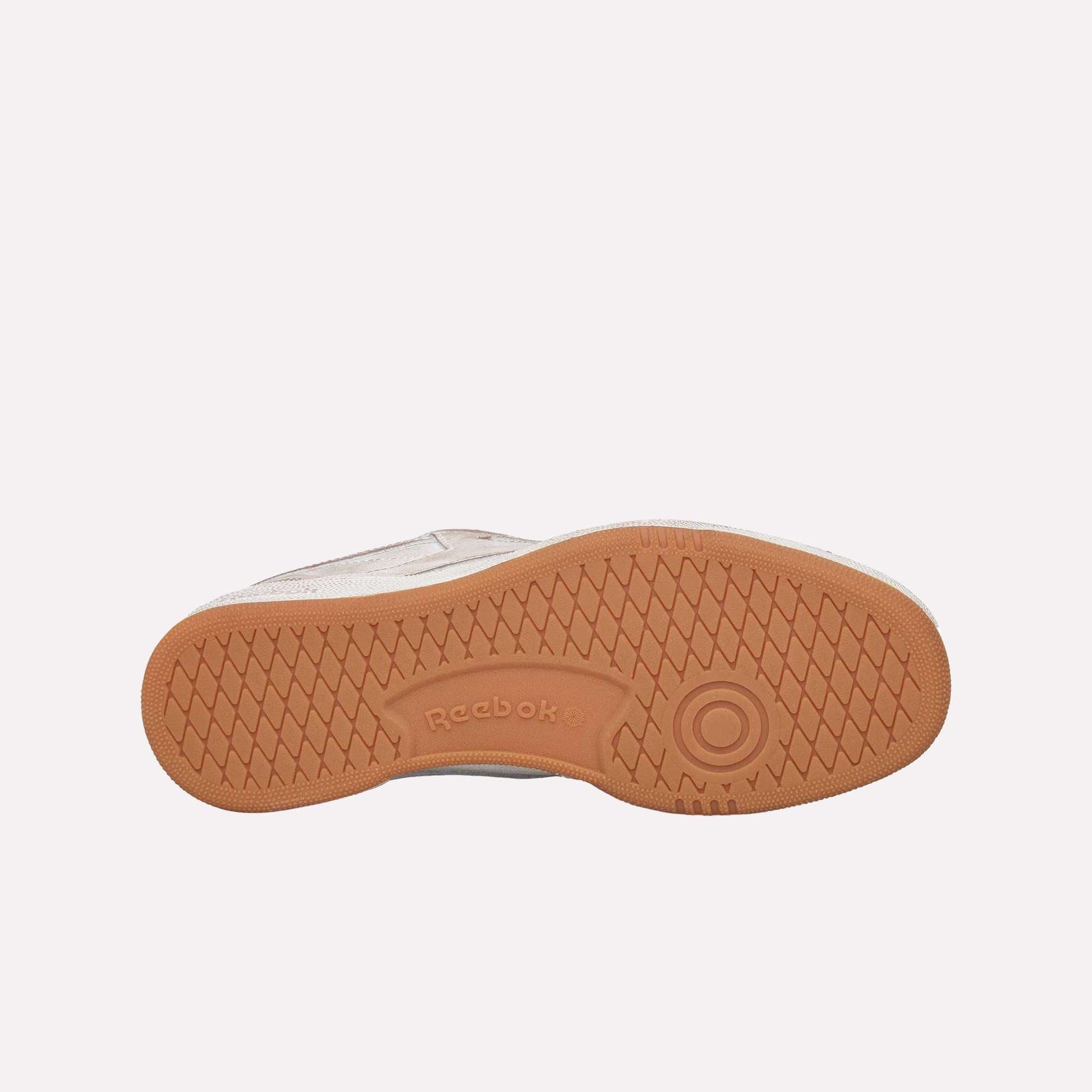 The image shows the sole of the Reebok Club C 85 Vintage, featuring a light brown rubber outsole with a diamond-textured tread pattern and an embossed Reebok logo—an iconic lifestyle classic.